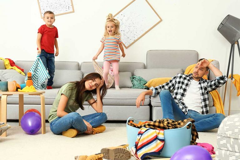 Genervte Eltern im Wohnzimmer der wie ein Spielplatz für Kinder aussieht